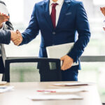 Image two business partners in elegant suit successful handshake together in front of group of casual business clapping hands in modern office.Partnership approval and thanks gesture concept